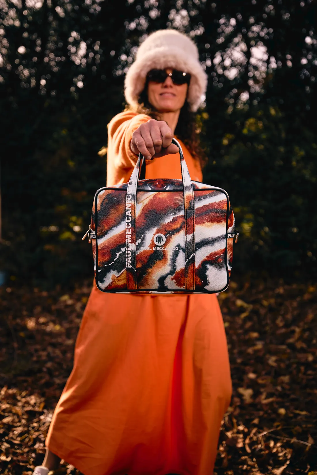 A woman in an orange dress and fur hat holding a colourful Paul Meccanico bag